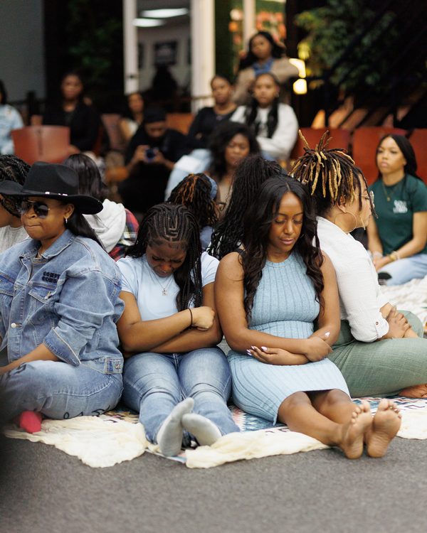 Women sitting close together on blankets with their heads bowed.